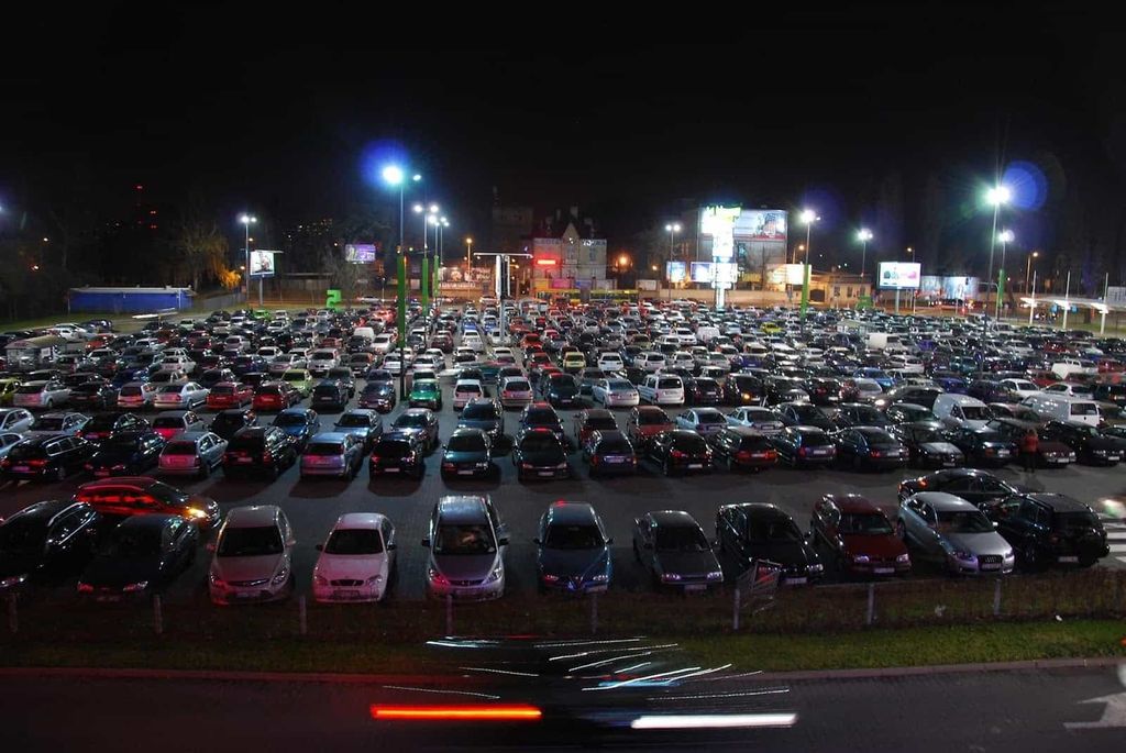 Duży oświetlony parking nocą pełen samochodów